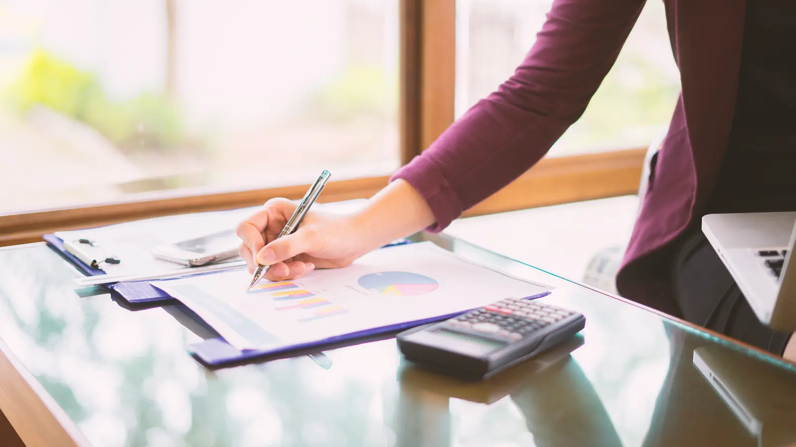 Investorin am Schreibtisch mit Diagrammen und Taschenrechner